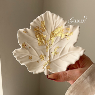 White leaf-shaped dish with gold leaf design held by a hand, brand 'Gold Leaf' visible.