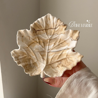 Hand holding a beige marble leaf-shaped bowl against a neutral background