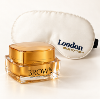 BROW DOCTOR London Brow Miracle Mask jar with a gold lid and clear glass base, shown in front of a white satin sleep mask with the London BROW DOCTOR logo.