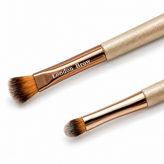 Two makeup brushes with rose gold ferrules and textured beige handles, featuring the brand name 'London Brow' engraved on the ferrule, set against a clean white background.