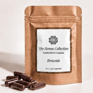A brown stand-up pouch labeled 'The Henna Collection London Brow Company Brownie' with several dark brown capsules placed in front on a light neutral background.
