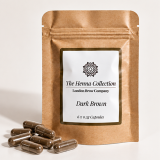 A kraft paper stand-up pouch labeled 'The Henna Collection London Brow Company Dark Brown' with several dark brown capsules placed in front on a clean white background.