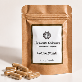 A stand-up kraft pouch labeled 'The Henna Collection London Brow Company Golden Blonde' with several brown henna capsules placed in front on a light neutral background.