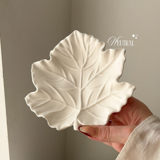 Natural colour leaf-shaped ceramic dish held by a hand against a neutral background